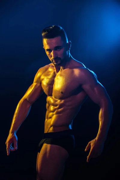 Athlete performs at competitions in black shorts with naked bare body against blue background. Man bodybuilder. Athletic man with biceps, shoulders, triceps, chest, abs, six pack. Male model sexy — Stock Photo, Image