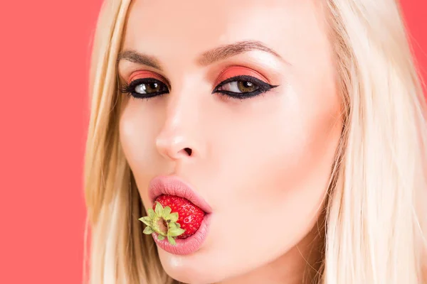 性感的金发女孩时尚化妆嘴里的美味草莓。肖像俏佳人草莓在粉红色的背景。草莓的女孩。性感俏皮女人草莓在嘴里 — 图库照片