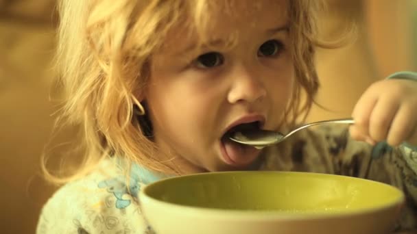 Reggeli gyermek eszik. Kisgyermek az egészséges táplálkozás. Aranyos fiú gyönyörű hajjal otthon asztalnál kanál zabkása, vagy a rizs. Gyermek étkezési zabkását tejjel. Koncepció egészséges reggeli gyerekeknek — Stock videók
