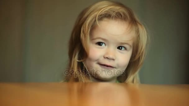 Smil 子のキッチン、テーブルでかわいい赤ちゃんの笑顔します。小さな子供は、自宅キッチンで幸せと笑顔です。歯と美しい髪を持つ少年の肖像画。緑の t シャツの話で幼児 — ストック動画