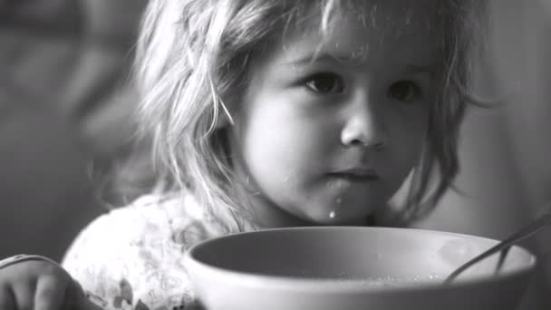 Child baby eats, plate of cereal on table for cute baby. Breakfast at home, baby dabbles and licks plate with his tongue. Baby food, black and white video. Baby health, delicious food for toddler — Stock Video