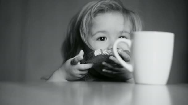 Το παιδί τρώει ψωμί και πίνει γάλα για πρωινό στο τραπέζι στην κουζίνα, βρεφικό φαγητό για υγιεινό γλυκό, όμορφο χαριτωμένο παιδί με μακριά μαλλιά. Μικρό παιδί αγόρι έχει νόστιμο πρωινό ή δείπνο για την υγεία — Αρχείο Βίντεο