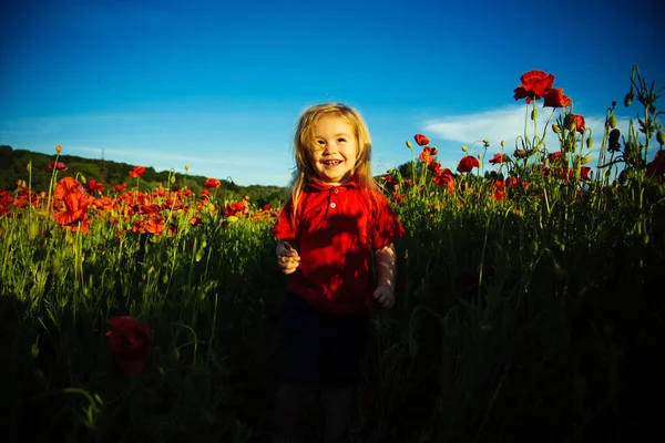 Cute baby, red flower and beautiful field. Happy childhood, sun and flowers, beautiful background. Children's clothing of red color. Summer holidays for children — Stock Photo, Image