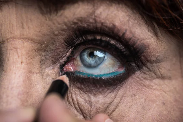 Μακιγιάζ για ηλικιωμένη γυναίκα. Μάτι της γυναίκας ηλικίας άνοιγμα, make-up artist ισχύει μαύρο μολύβι κάτω από τα βλέφαρα και τις βλεφαρίδες. Ομορφιά για τους ηλικιωμένους. Όμορφη γυναίκα για 50, 60 ετών. Η γιαγιά στο σαλόνι ομορφιάς — Φωτογραφία Αρχείου