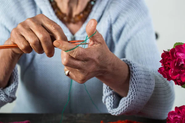 Grandmother knits woolen threads and knitting needles, wool for winter. Hand made. Old woman knits, beautiful grandmother in blue warm jacket knits woolen product, hobby in old age with flowers