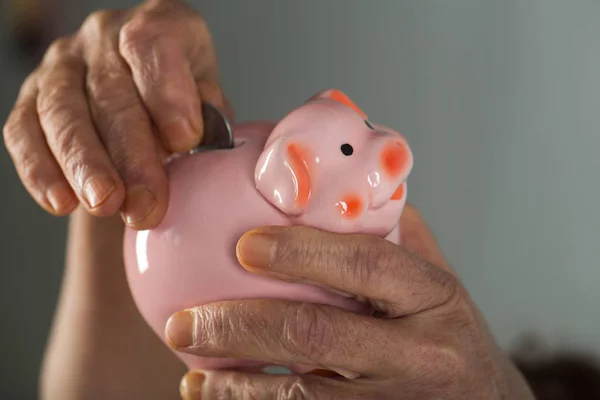 Застава свинячого банку, стара жінка кидає монету в іграшку для заощаджень свині, заощаджуючи на старість, щоб заощадити гроші на тихий старість. Вік і гроші. Економте гроші на пенсію, пенсійний фонд, бідну бабусю — стокове фото
