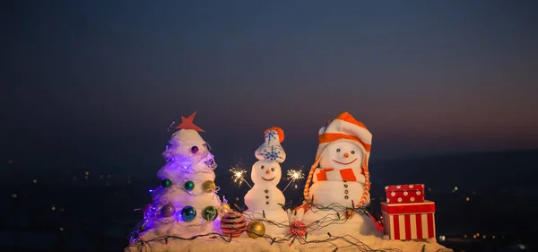 Noche de Navidad, montañas con muñecos de nieve desean Feliz Navidad y Feliz Año Nuevo. Vacaciones familiares en las montañas. Nieve en las montañas. Decoraciones navideñas. Muñeco de nieve con luces Bengala — Foto de Stock