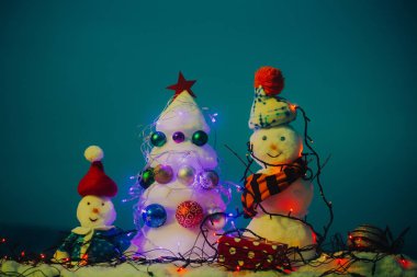 Seni Noel ve yeni yıl tebrik. Kar heykel neşeli duygular. Aile için tebrik kartı. Kar giyen şapka, ceket ve eşarp heykeller. Noel ağacı ve kardan adam garland ile kaplı