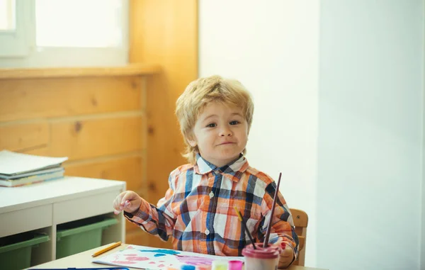 Pojke ritar ljus bild på barnens bord. Söt ung konstnär ler och tycker om kreativitet. Lycklig barndom och känslomässiga konst klass — Stockfoto