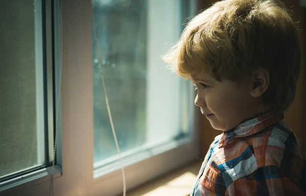 Niño esperando a los padres y mira impacientemente en la ventana. Triste chico lindo cerca de la ventana en un día lluvioso, esperando y la esperanza — Foto de Stock