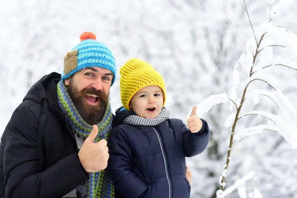 Μπράβο από πατέρα και γιου. Γενειοφόρος άνδρας και χαρούμενα ευτυχισμένο αγόρι χαμογελά μαζί και δείχνει δάχτυλο σε φόντο του χειμώνα πάρκο κοντά στο χιονοδρομικό κέντρο. Σκιέρ σε χρωματιστά καπέλα. Χειμερινά σπορ — Φωτογραφία Αρχείου