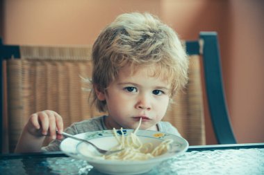 Bebek maması. Şirin çocuk spagetti yiyen ve kameraya benziyor. Aç çocuk iyi iştah ile öğle yemeğini yiyor. İtalyan gıda ABD. Çocuk beslenme, çatal bıçak takımı
