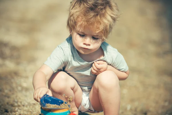 Serious emotional child builds a sand castle, works with building materials, future builder. Developing game, game therapy, psychological therapy with sand. Pleasure of summer holidays on beach — Stock Photo, Image