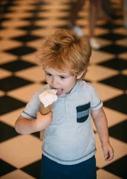 かわいい幼児少年アイス クリームを食べるします 子供と一緒にアイスクリームを食べるとカフェを歩いて汚れた顔 シャツにかわいい金髪の少年を味わう彼の砂漠 黒と黄色のチェスの床の背景 — ストック写真