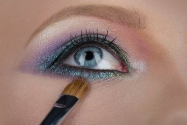 Gözler için makyaj. Kadın mavi gözlü yakın çekim. Güzel kozmetik yüz kadın baştan çıkarıcı görünüyorsun. Mavi ve pembe gölgeler için fırça. Güzel renk, kaşları ve seksi kadın güzelliğinin öğrenci