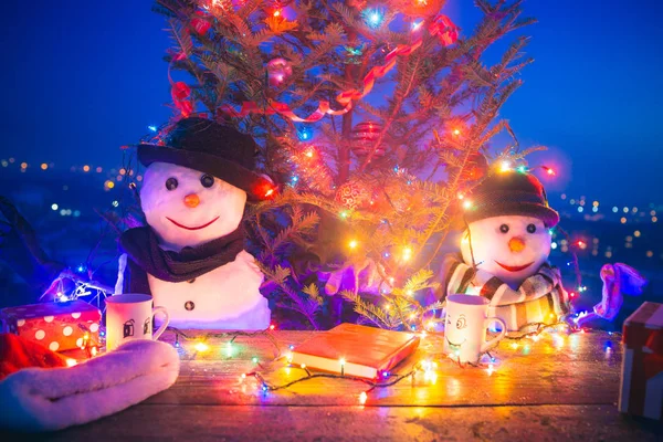 Fiesta de Navidad, regalos cerca del árbol de Navidad y familia en la mesa. Hermoso fondo colorido para vacaciones. Muñecos de nieve en sombreros — Foto de Stock