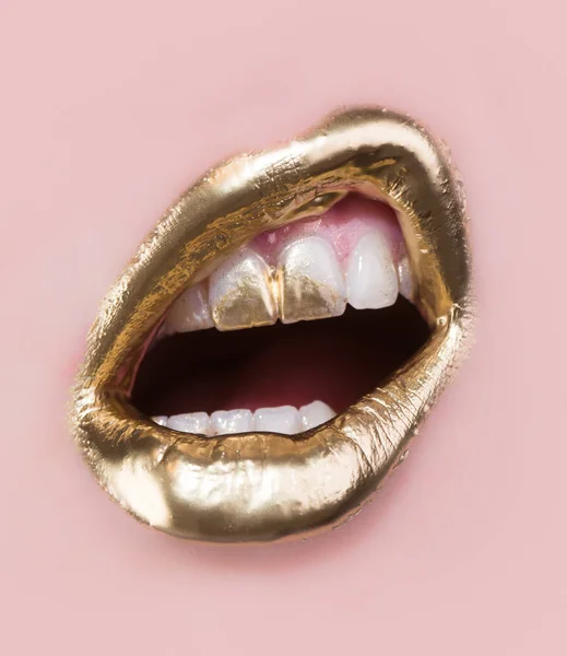 Os lábios dourados fazem as pazes. Pintura dourada em lábios e dentes. Boca aberta e dentes brancos isolados sobre fundo rosa. Parte do rosto rico coberto de ouro. Maquilagem moderna para mulheres. Sensual conceito de luxo dourado — Fotografia de Stock