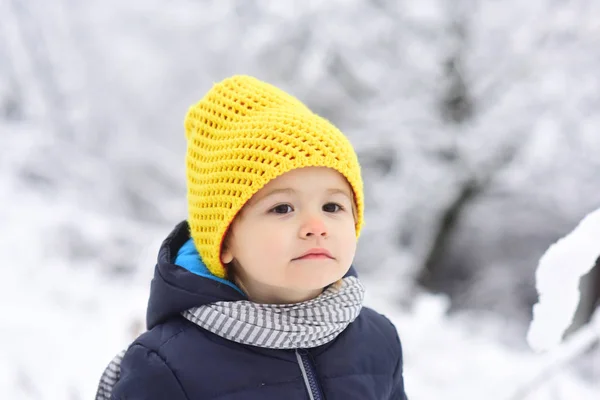 Αξιολάτρευτο παιδί σε χιονισμένο τοπίο, λευκό φόντο του δάσους. Χαριτωμένο αγόρι με κίτρινο πλέξιμο καπέλο Κοιτάξτε κάπου μακριά, στοχαστικό βλέμμα του παιδιού. Πορτρέτο σοβαρό όμορφος παιδάκι περιμένοντας την άνοιξη — Φωτογραφία Αρχείου