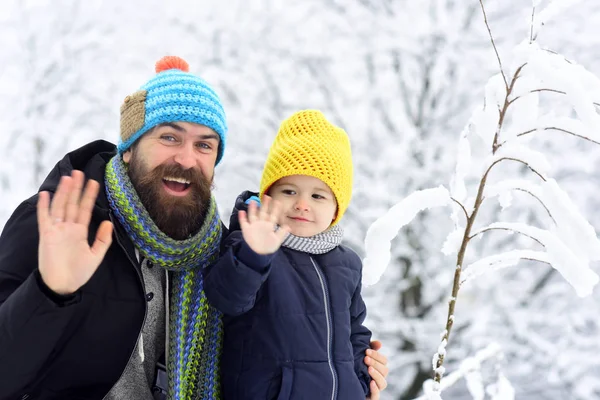 Πατέρας και γιος στο σύμπλεγμα δομών, κουνώντας γειά σου. Χειμερινές διακοπές στα βουνά. Ζεστά ρούχα, πολύχρωμα καπέλα και κασκόλ. Χαριτωμένο αγόρι και γενειοφόρος πατέρας λέει γειά σου στα βουνά. Οικογένεια με τα πόδια κατά τη διάρκεια της μέρα του χειμώνα — Φωτογραφία Αρχείου