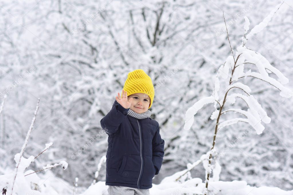 Cheerful boy waving his hand to camera, hello hi concept. Cute little funny child in colorful winter clothes having fun with snow outdoors. Active outdoors leisure with children in winter