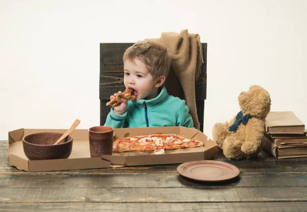 Criança come pizza na mesa de madeira isolada no fundo branco. Comida rústica caseira na Itália. Almoço de rapaz com brinquedo de urso. Prato de glúten. Comida deliciosa para crianças pré-escolares. Jantar e fast food — Fotografia de Stock