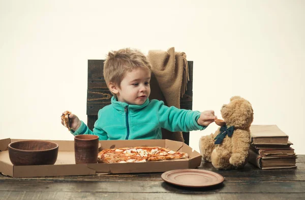 Comida de bebé. A criança está alimentando o urso brinquedo. O miúdo partilha comida com o amigo. Pizza e mingau para o almoço. Entrega de pizza. Pizza numa caixa. Almoço saboroso no jardim de infância ou na escola. Comida por encomenda. Pizzaria em casa — Fotografia de Stock