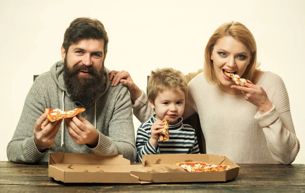 Happy family eating pizza on the wooden table. Family takes pieces of pizza. Happy lovely family eating pizza. Young mother and her little son eating pizza and having fun with husband. Family kitchen