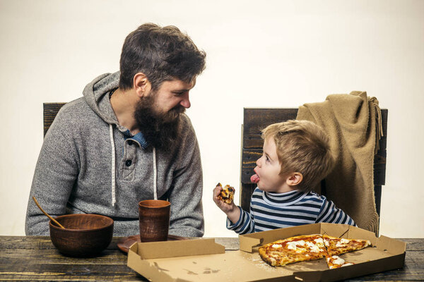 Funny child shows tongue to father at dinner. Family dinner, games and heart conversation. Education and friendship with the child. Cheerful delicious pizza in the family kitchen. Modern dad