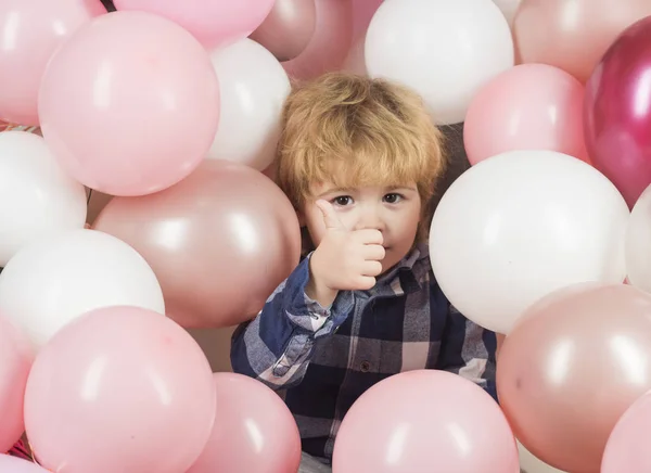 Мальчик на вечеринке показывает большие пальцы вверх. Красивый ребенок среди розовых шаров счастлив подарками и счастливым детством. Дети закрывают лицо. Белые и розовые шары украшают мероприятие. Открытие магазина детских игрушек — стоковое фото