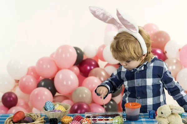 Draw Easter eggs. Cute baby is making scenery for the holiday paint. Children room before Easter. Handmade egg against the background of balloons. Child before Easter preschooler