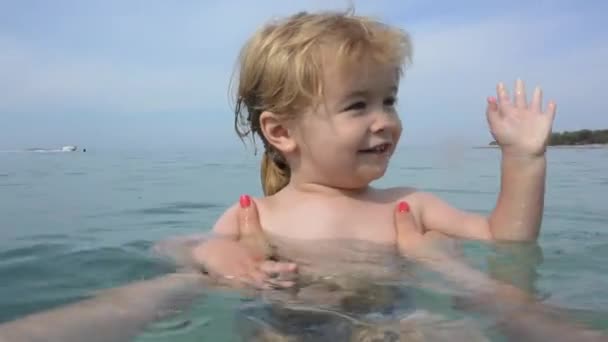海の手を振って子供こんにちは 夏を楽しむ モーターの手で楽しい時を過します 夏休みに水泳のレッスン 赤ちゃんと一緒にビーチで夏の残り 水の美しい子供は 観光の喜び — ストック動画