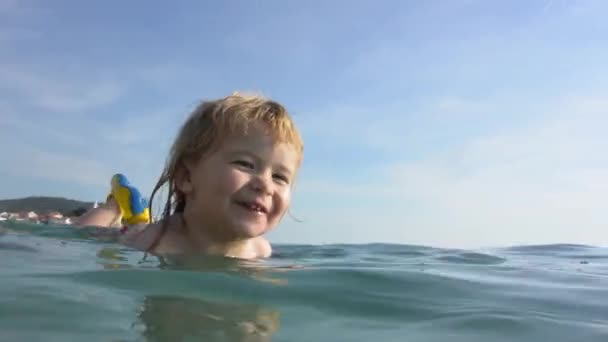 幸せな子は笑うし 海で泳ぐ 子供の顔に笑顔します 赤ちゃんは お母さんと一緒にビーチに海で泳ぐ学習です 観光と健康な子供時代の幸せな夏休み 大きな子供の笑顔 — ストック動画