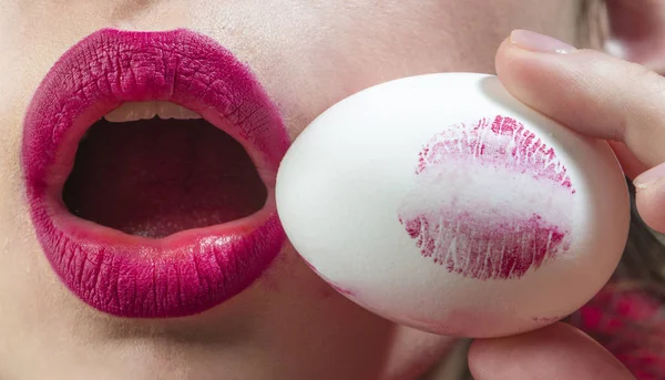 Easter egg concept. Lipstick print on round egg. Female mouth and red fashionable lipstick. Beautiful symbol of femininity life. Woman or girl holding an egg and kiss. Cosmetics for housewife. Food
