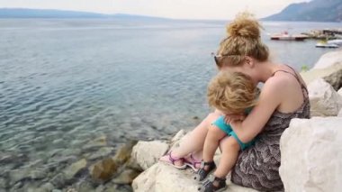 Aile tatil, mutlu anne oğluyla deniz desteklemek. Güzel yaz hava büyük plaj. Anne ve çocuk ile Denizi tatil. Genç mutlu güzel anne ve küçük oğlu sarılma. Olumlu duygular