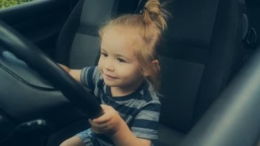 Direksiyon simidi, sürücü kursu, hobi olarak sürüş. Uzun saçlı çocuk arabaları seviyor. Ön koltukta bir baba arabada güzel bir çocuk. Emanet direksiyonda. Binek otomobil çocuklar için. Bebek mi