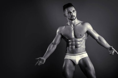 Adam güneşlenmek için poz veriyor. Siyah beyaz fotoğrafçılık. Yakışıklı kaslı adam, vücut geliştiren, siyah arka planda poz veren. Stüdyoda çıplak bir erkek modelin portresi..