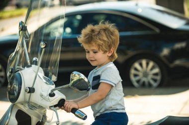 Nakliye aracı. Küçük motorcu. Çocuk bir motosikletin üzerinde oturuyor. Bisiklet aynası. Otoparkta mutlu bir sürücü var..