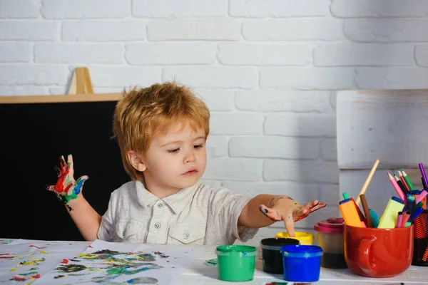 Finger painting. The boy touches multi-colored paints with his fingers. Drawing with vibrant colors. Early development. School for kids.