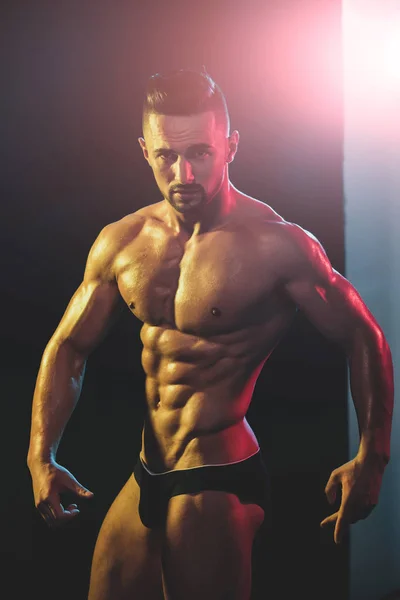 Homme athlétique fort montre le corps et les muscles abdominaux sur fond sombre. Jeune beau bodybuilder avant les compétitions sportives. Homme nu avec un corps sexy et chaud. Attrayant gars pose avec un corps parfait . — Photo