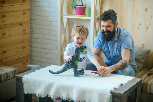 Adorable little child plays with his bearded father with plastic dinosaurs. Son and father play in battle fight between big tyrannosurus and little dinosaur. Interesting gift for child, present.