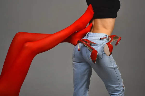 Corpo de mulher magro em jeans torm azul e camisa preta com saltos vermelhos no fundo cinza. Pernas em meias vermelhas tocar cintura nua de outras meninas. Conceito homossexual de duas meninas juntas. Vida lésbica . — Fotografia de Stock