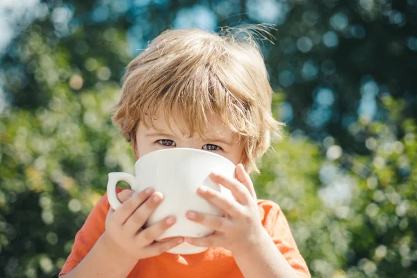 Beaux yeux d'enfant. Un garçon boit du lait ou du thé dans le jardin. Aliments sains pour bébés . — Photo