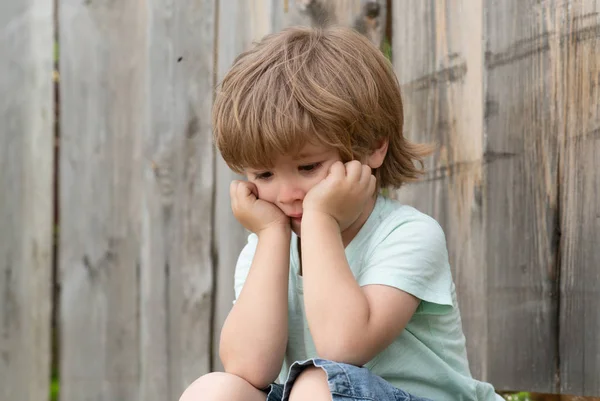Szomorúság. Szomorú fiú. Egy magányos gyerek ül egy fa kerítés mellett. Frusztráció. Szomorú érzelmek. Tapasztalatok. Gyerekpszichológia. Magányosság. — Stock Fotó
