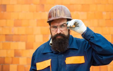 Güvenlik ekipmanı olan bir işçi. Kask takan, eldiven takan, koruyucu eldiven takan bir adam. İnşaat koruma giysileri. Kızgın müteahhit çekiçle yok etmeye hazırlanıyor..