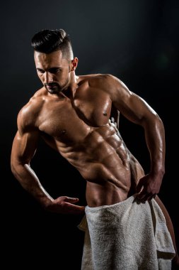 Handsome young strong man. Stripped guy with white towel on dark background. Naked bodybuilder with towel.