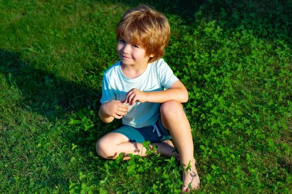 El sol de primavera. El chico se sienta en la hierba verde del parque. Niño en la naturaleza. Humor de primavera. Sol y niño. Verano pronto . — Foto de Stock