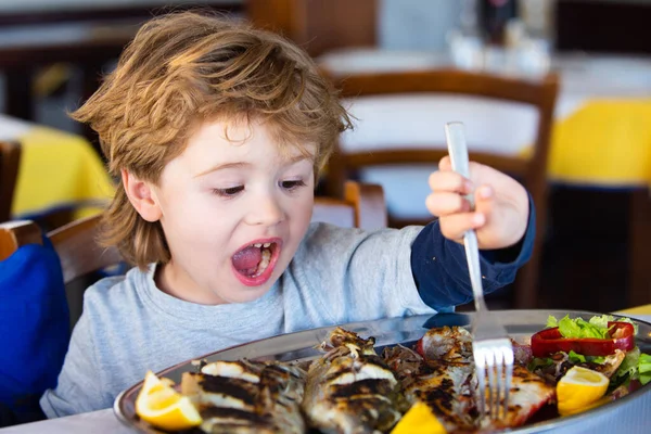 興奮した子供はレストランで海魚を食べる。地中海料理。子供のための健康食品。ヨウ素の源として昼食のための海の魚。カフェの子供が昼食を取っている. — ストック写真