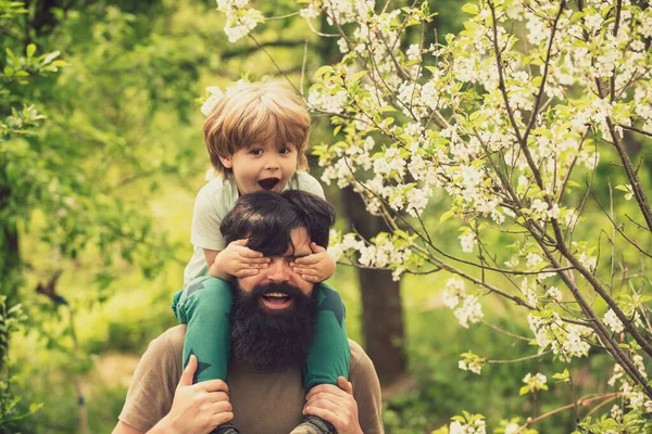 Χαρούμενο ενθουσιασμένο αγόρι με γενειοφόρο πατέρα. Οικογενειακό περπάτημα στο φόντο της φύσης. Την άνοιξη μαζί. Τα παιδιά χαμογελούν. Οικογενειακή διάθεση. — Φωτογραφία Αρχείου
