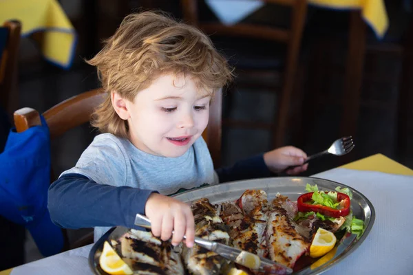 Счастливый мальчик ест рыбу с ножом и вилкой в ресторане. Манеры. Обед в кафе. Детское и здоровое питание. Школьник и обед. Детский аппетит . — стоковое фото