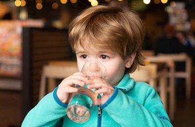 Bir çocuk kafede su içiyor. Çocuklar için saf su. İçelim. Çocuk bir bardak su tutuyor..